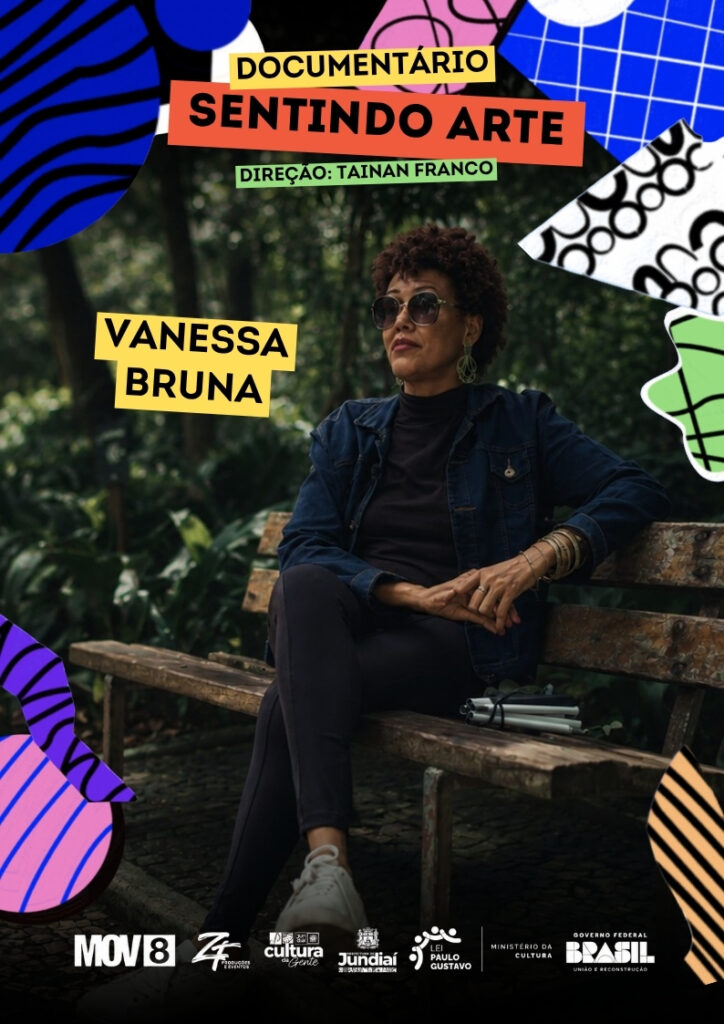 #PraCegoVer: Cartaz de divulgação do documentário “Sentindo Arte”. A imagem mistura fotografia e colagem gráfica, com formas abstratas coloridas nas bordas, em azul, rosa, verde, preto e branco. No centro, aparece uma mulher sentada em um banco de madeira, em uma área verde com árvores ao fundo. Ela usa óculos escuros, jaqueta jeans, roupa preta, tênis branco e acessórios nos braços e nas orelhas. Ao lado dela, sobre o banco, há uma bengala dobrável. À direita da imagem há uma faixa amarela com o nome “Vanessa Bruna” em letras pretas. Na parte superior, em faixas coloridas, está escrito “Documentário Sentindo Arte” e, abaixo, “Direção: Tainan Franco”. Na parte inferior, há uma faixa escura com os logotipos da MOV8, ZF Produções e Eventos, Cultura Jundiaí, Prefeitura de Jundiaí, Lei Paulo Gustavo, Ministério da Cultura e Governo Federal Brasil – União e Reconstrução.